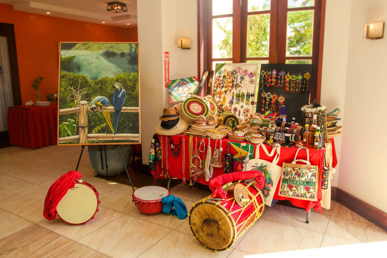A display of Guyanese crafts, a painting of macaws, beadwork and traditional drums