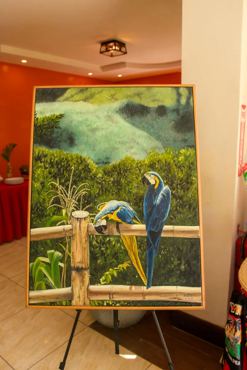 A painting of two blue-and-yellow macaws perched on a wooden fence